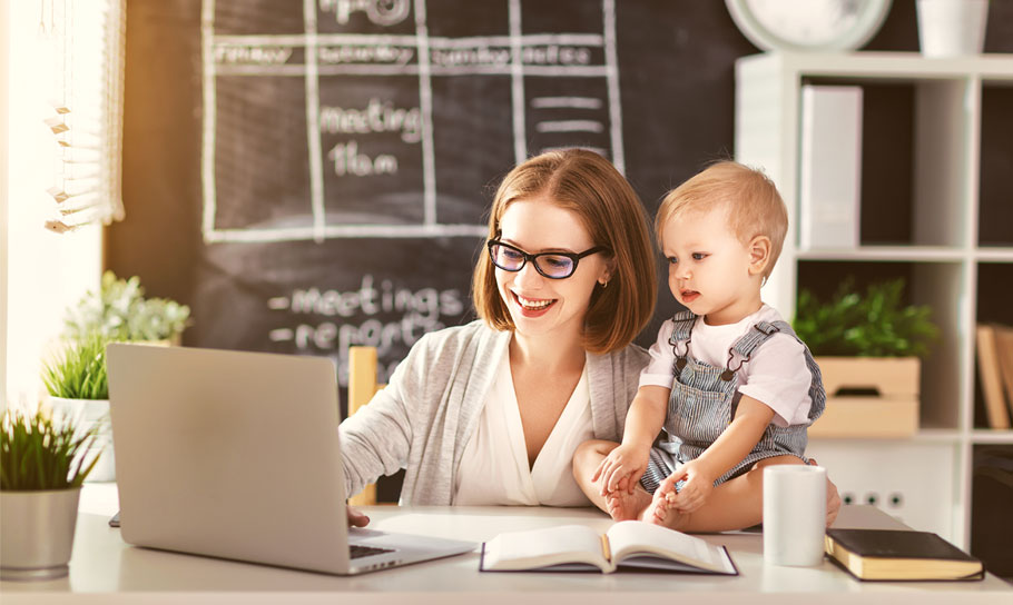Woman working from home on a laptop with her child sitting beside her