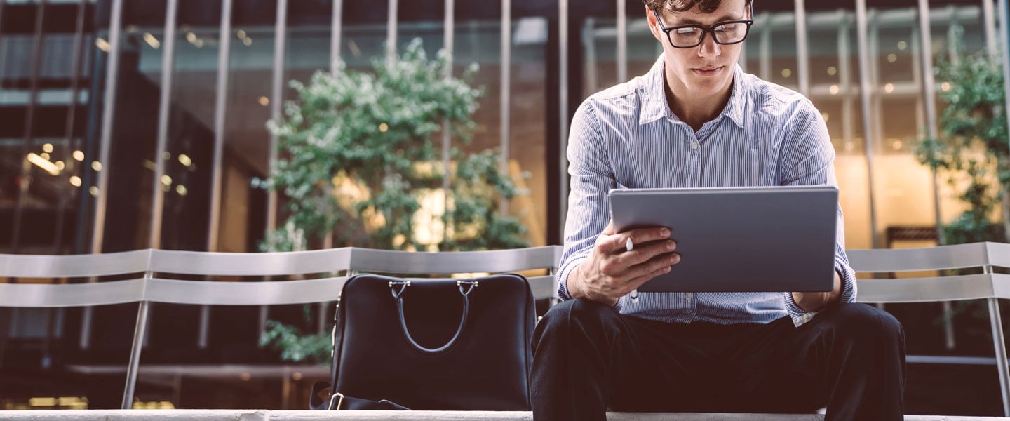 A man sat on a bench while he reads his tablet