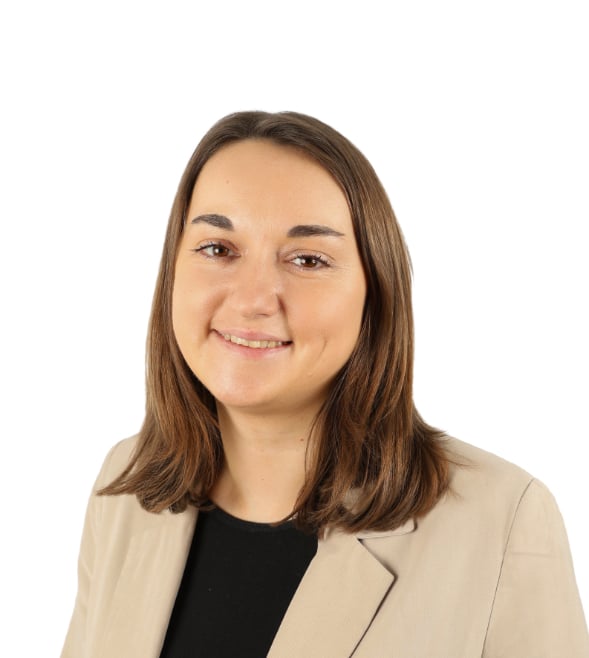 A woman with short brown hair looks into the camera and smiles for a corporate headshot. She is wearing a black top and beige blazer.