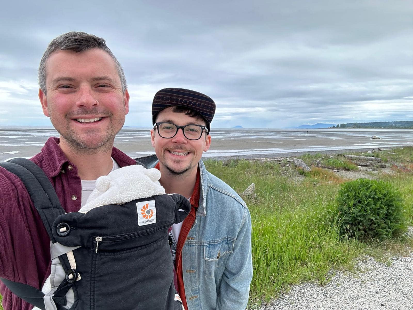 Two men are photographed on a walk outdoors, with their newborn child.