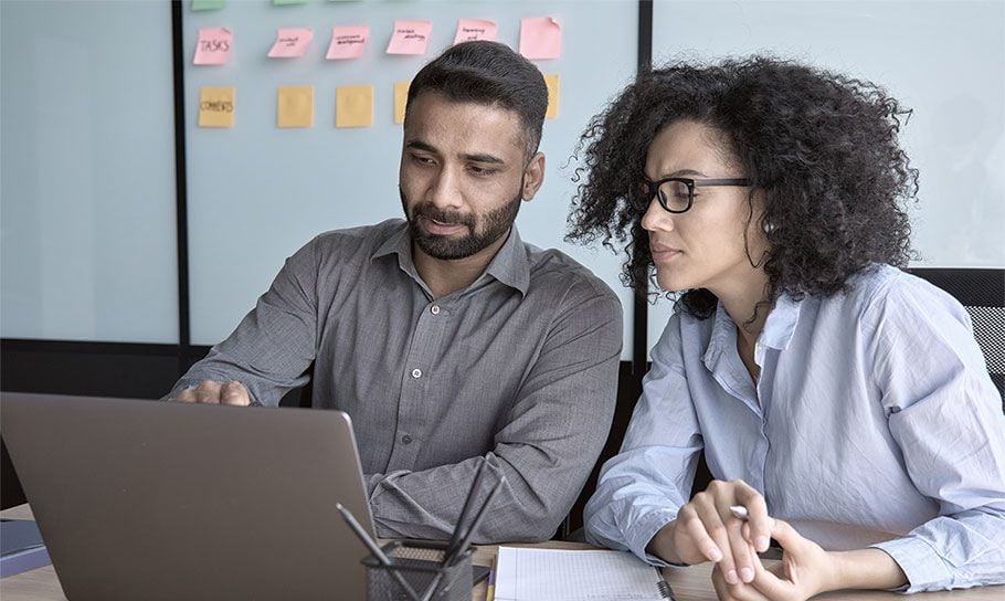 Male colleague showing female colleague data on laptop